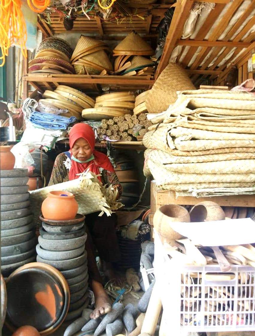 Seorang pedagang alat rumah tangga tradisional sedang menunggui dagangannya sambil menganyam di pasar tradisional Desa Gabus, Kecamatan Gabus, Pati, Jawa tengah,  Sabtu (7/9/2019). Hingga saat ini penjualan alat-alat rumah tangga tradisional berbahan baku bamboo, tanah liat dan kayu masih bertahan.